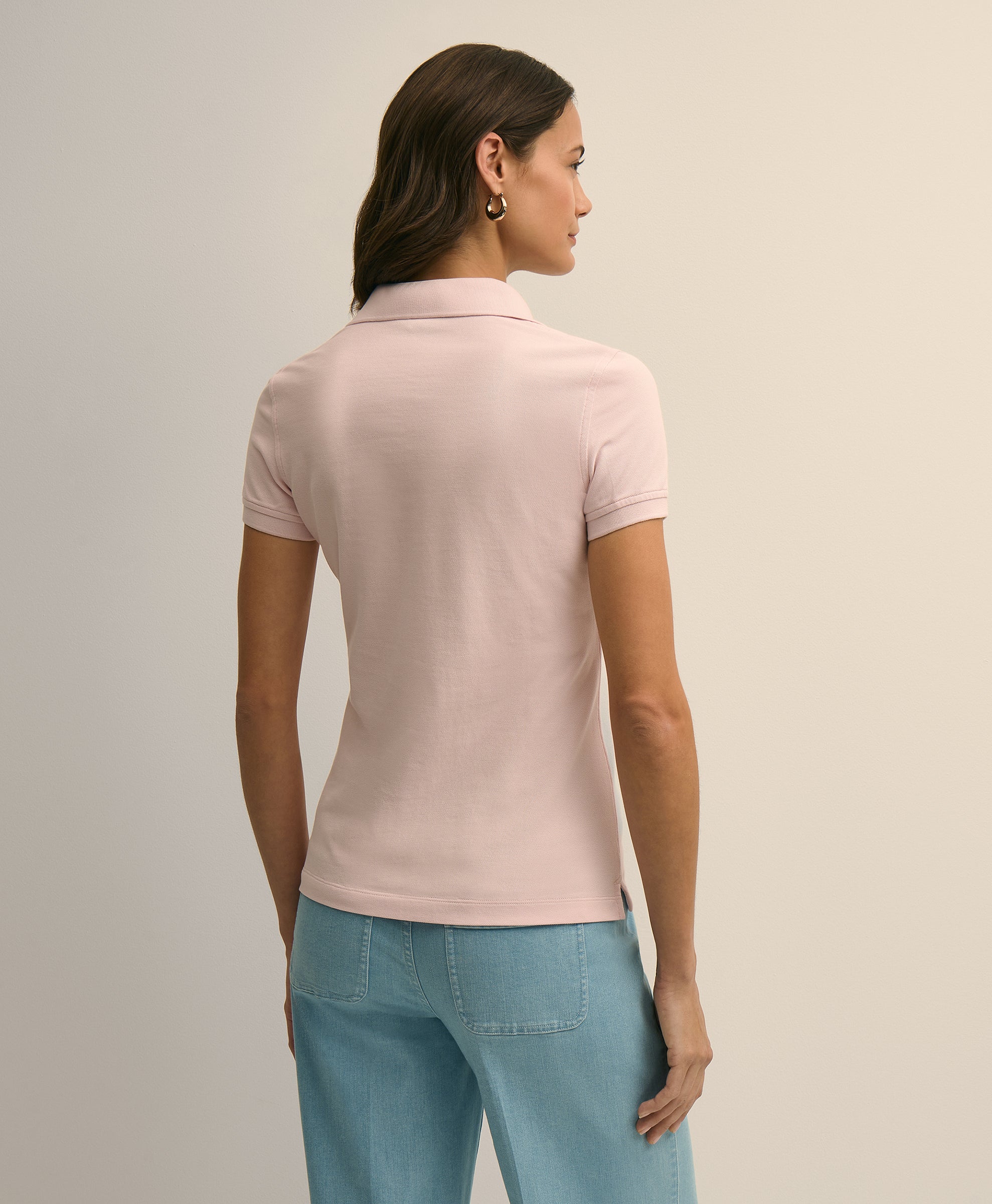 Woman wearing a light pink polo shirt and blue jeans