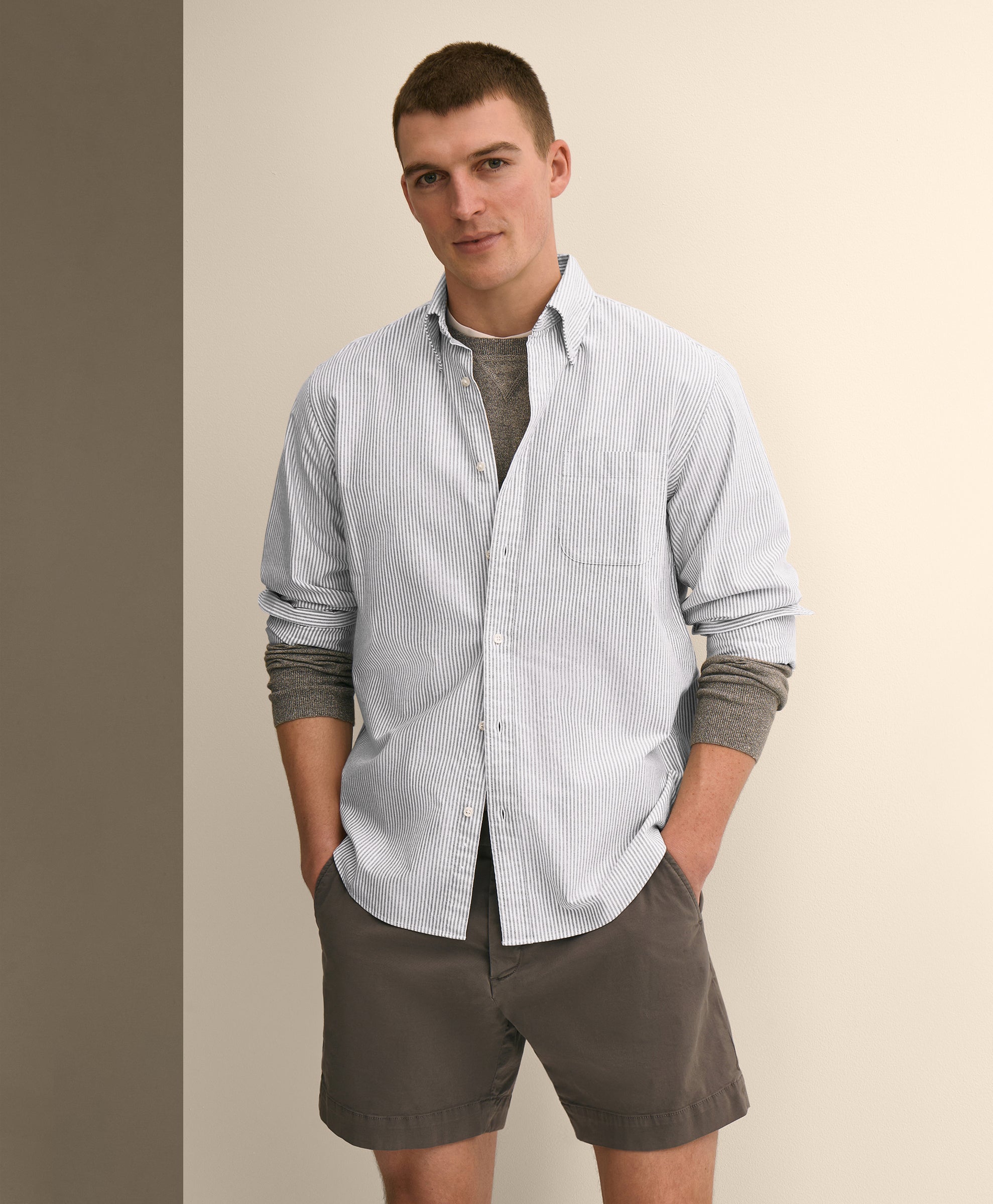 Man wearing a light blue striped shirt with rolled-up sleeves and brown shorts