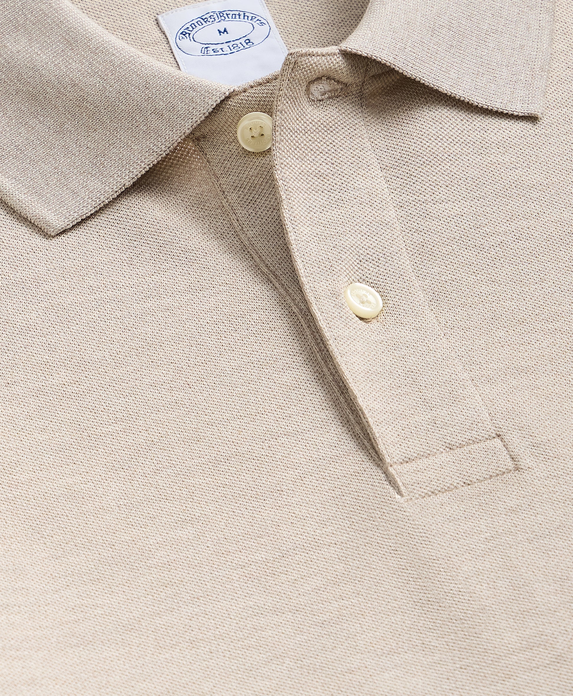 Close-up of a beige shirt with buttons and a brand label.