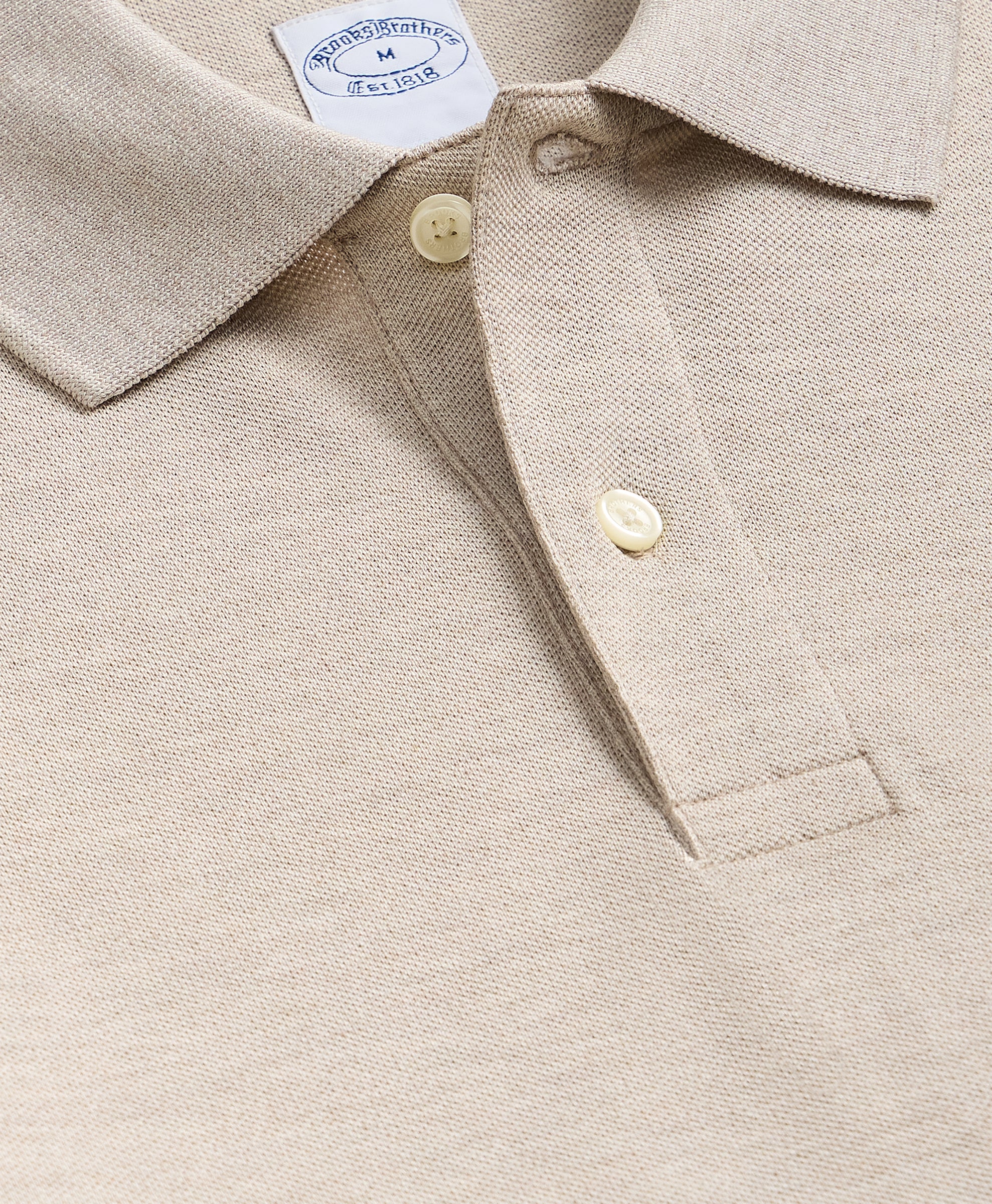 Close-up of a beige shirt with buttons and a brand label.