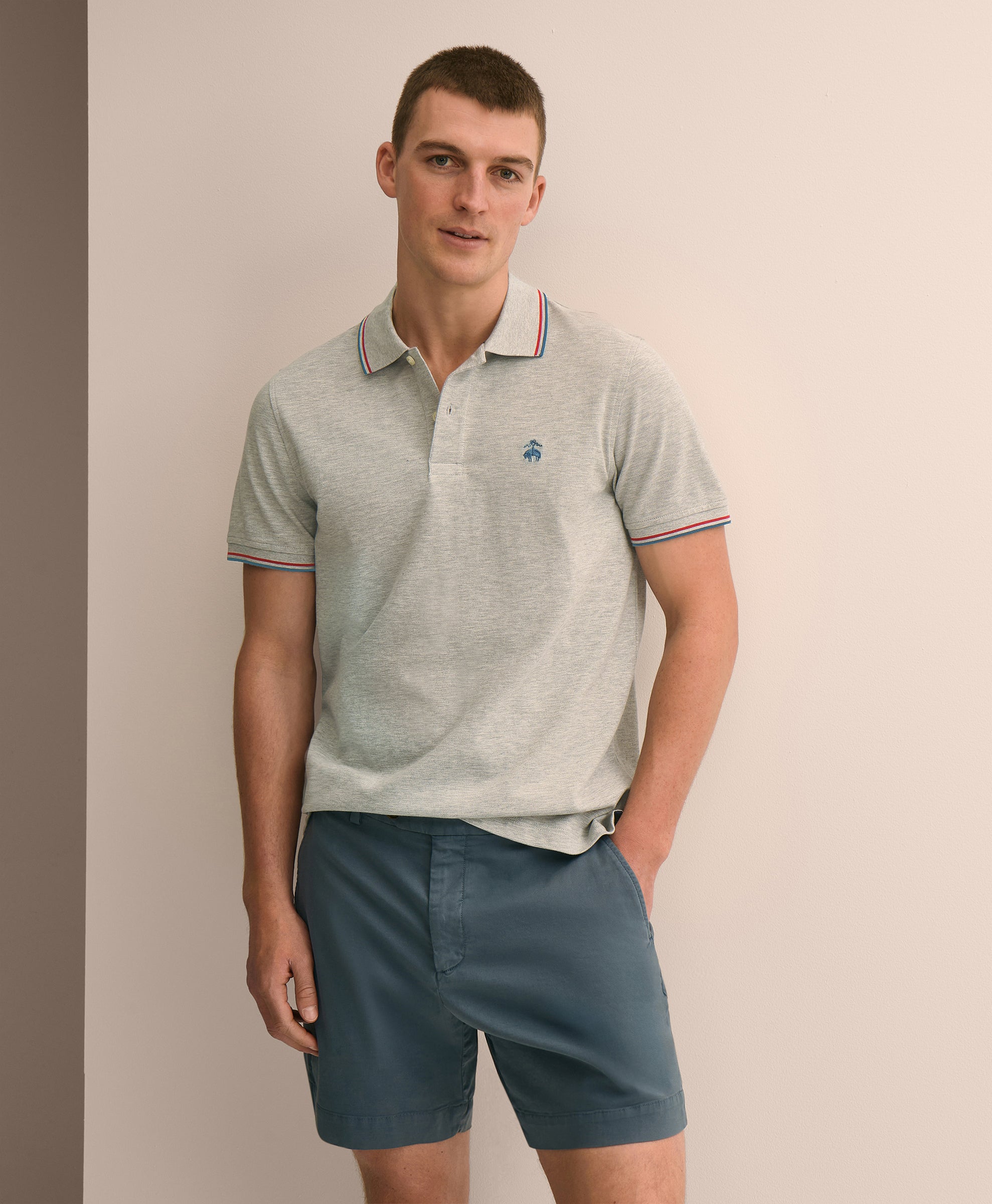 Man wearing a light gray polo shirt with a small logo and dark blue shorts