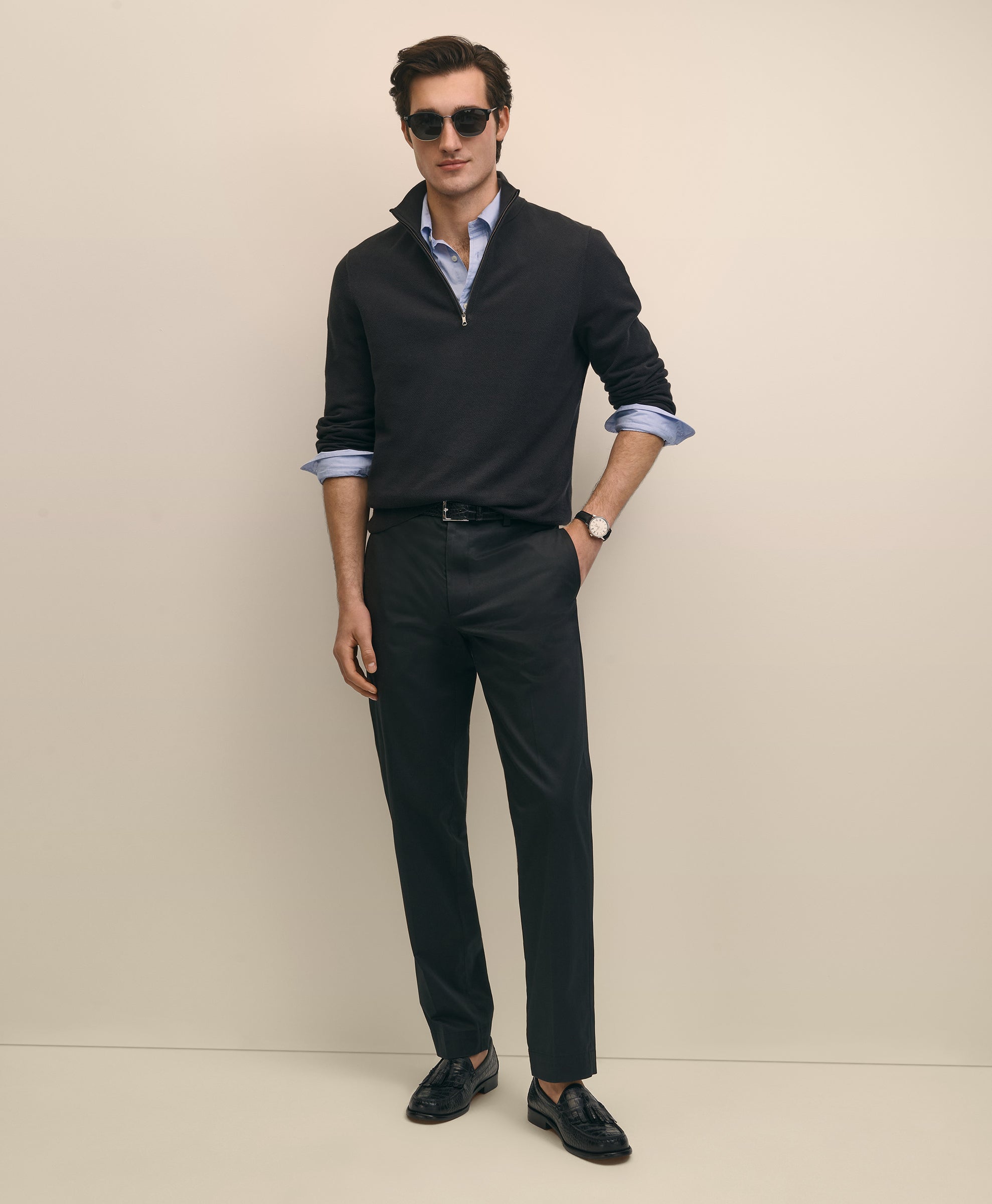 Man wearing a dark sweater, light shirt, black pants, and sunglasses