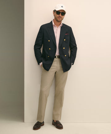 Man wearing a navy blazer with gold buttons, light pink shirt, beige pants, and dark shoes