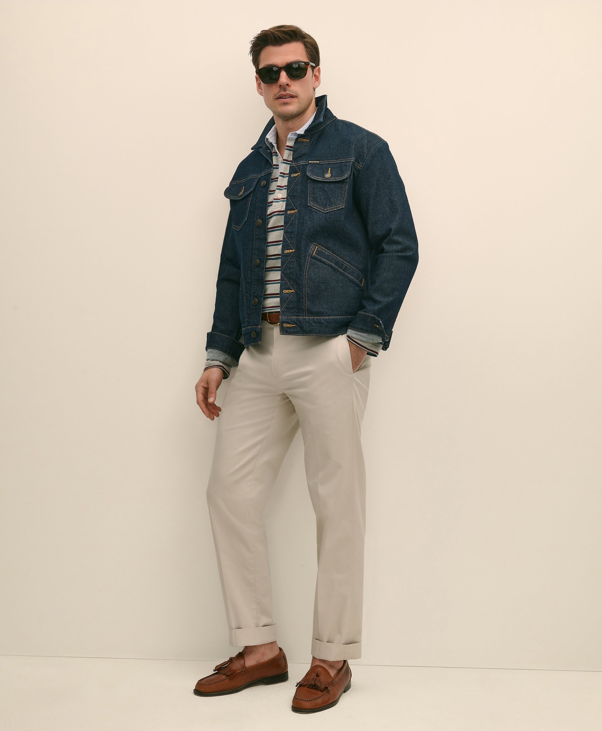 Man wearing a denim jacket, striped shirt, beige pants, and brown shoes