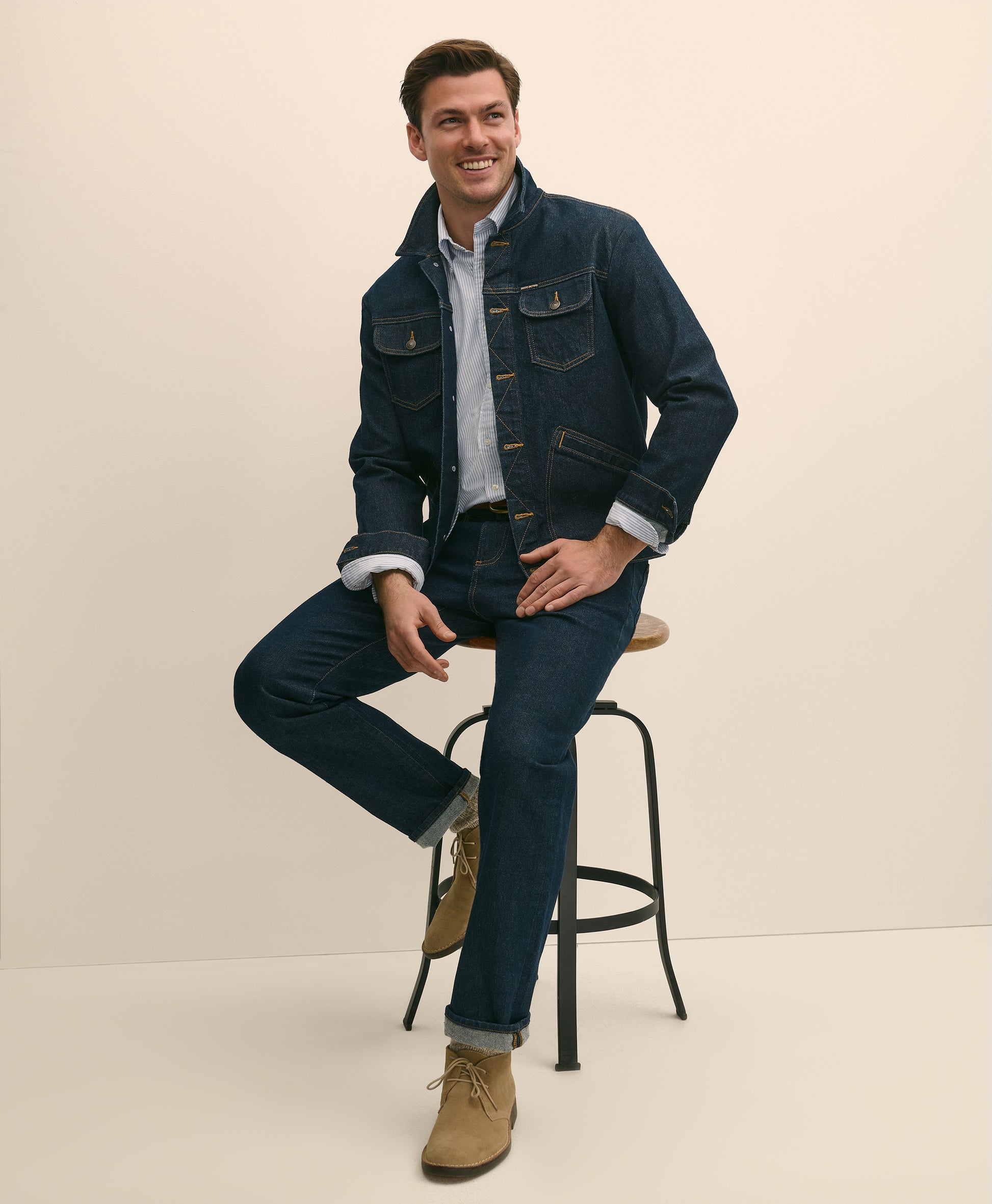 Man wearing a denim jacket and jeans sitting on a stool