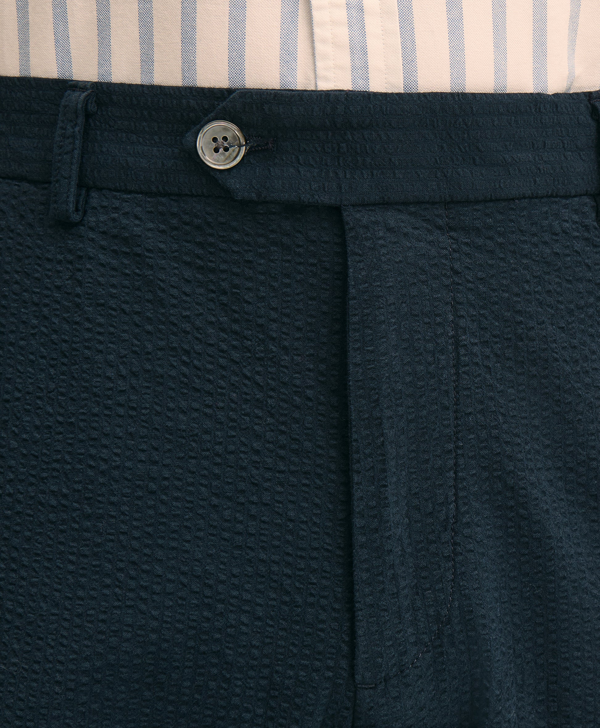 Close-up of navy pants with a button detail, featuring a striped shirt