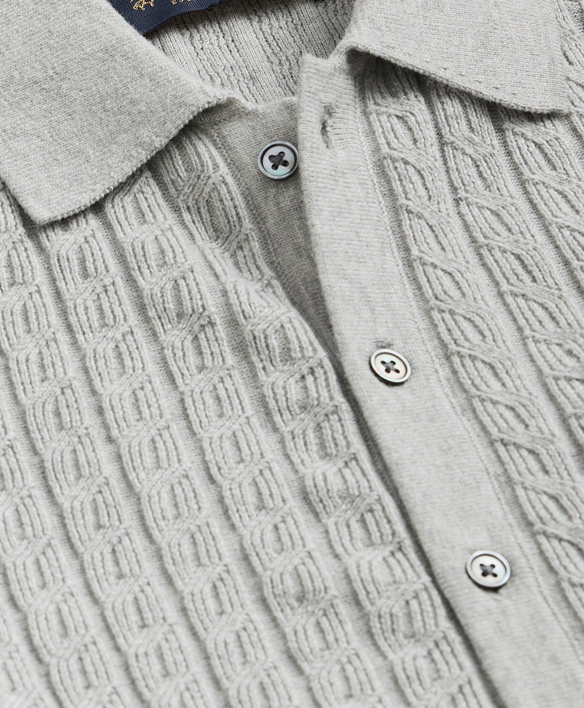 Close-up of a light gray cable-knit sweater with buttons