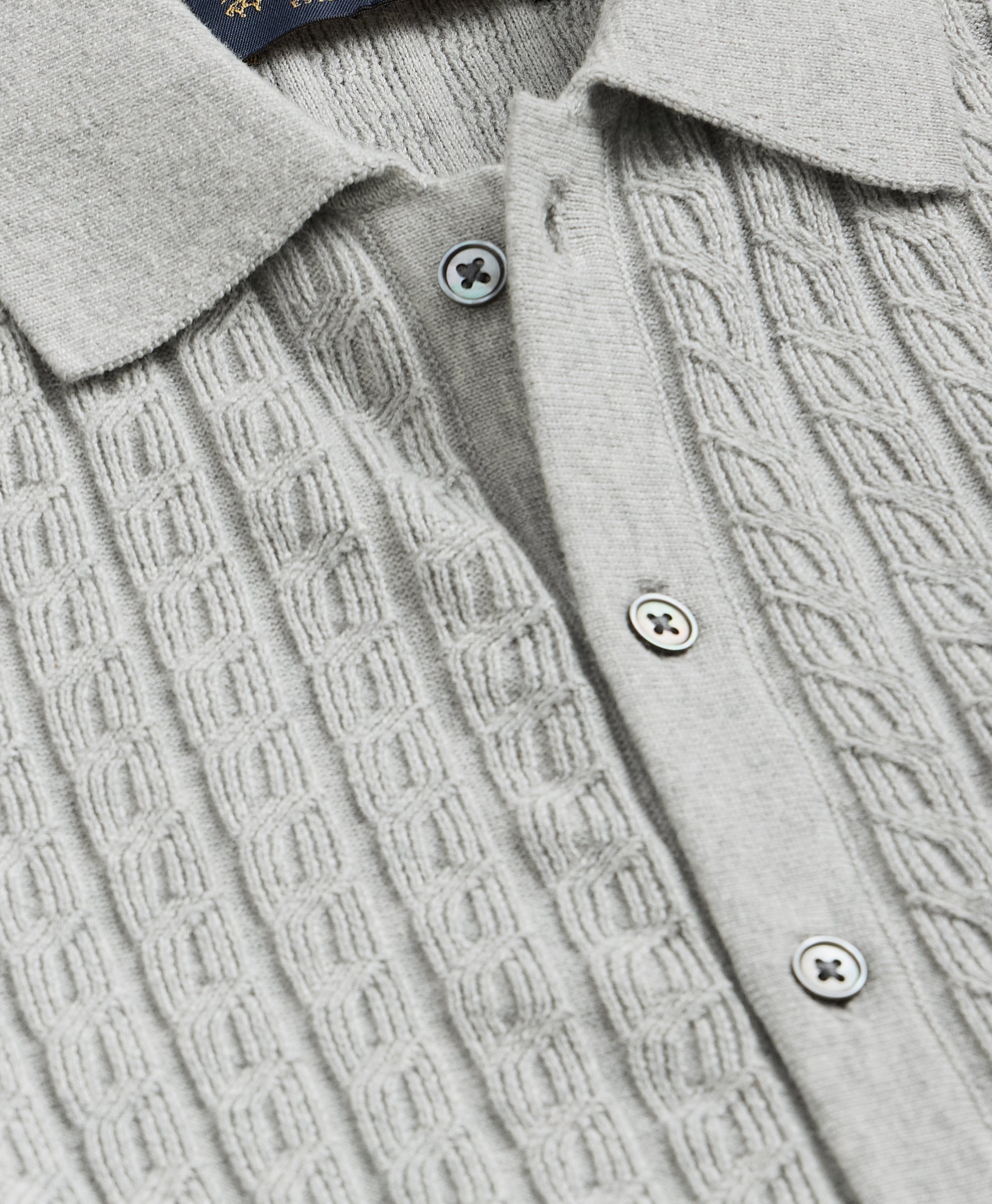 Close-up of a light gray cable-knit sweater with buttons