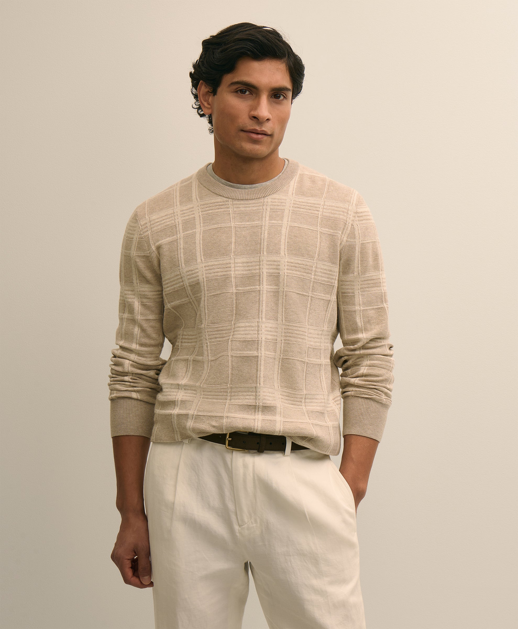Man wearing a beige checkered sweater and white pants