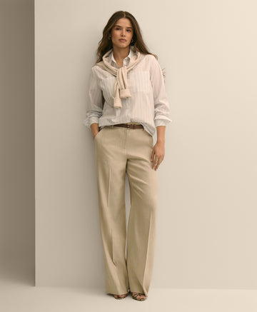 Woman wearing a light-colored blouse with a scarf and beige pants